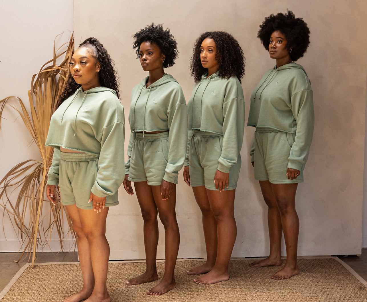 Four women wearing matching green outfits standing in a row against a neutral background.