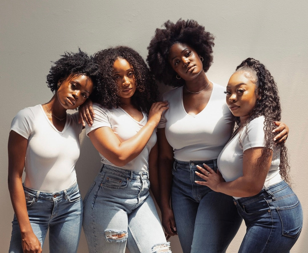 Four women wearing white tops and blue jeans posing together against a neutral background