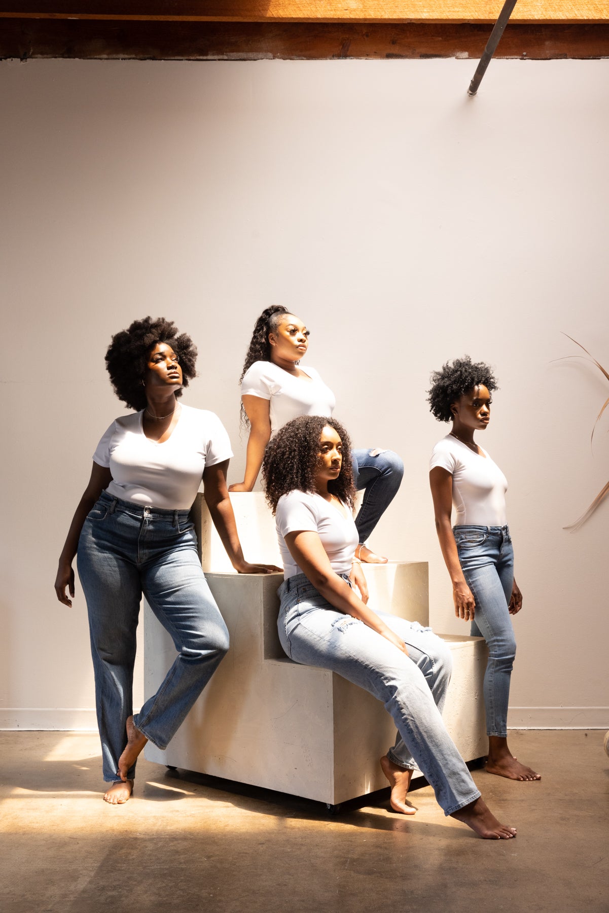 Four women sitting on a white bench against a plain wall.